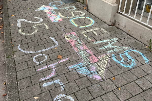 Das Bild zeigt Wegweiser zu QPS und zur EMS, die mit Straßenkreide auf dem Gehweg gezeichnet wurden.