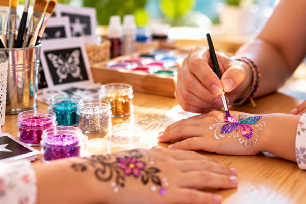 Das Bild zeigt wie ein Glitzertattoo auf eine Kinderhand gemalt wird.